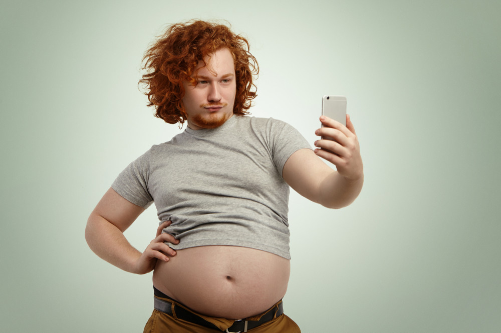 Mann macht ein Selfie von sich in einem bauchfreien T-Shirt.